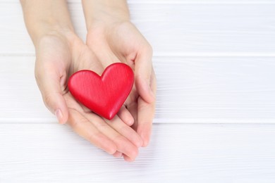 Photo of Woman holding red heart at white wooden table, closeup. Space for text