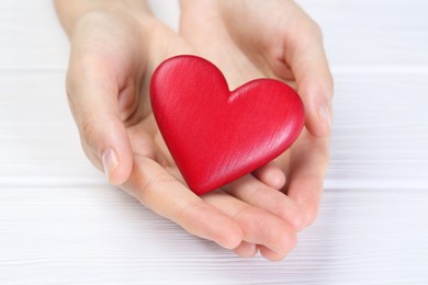 Photo of Woman holding red heart at white wooden table, closeup