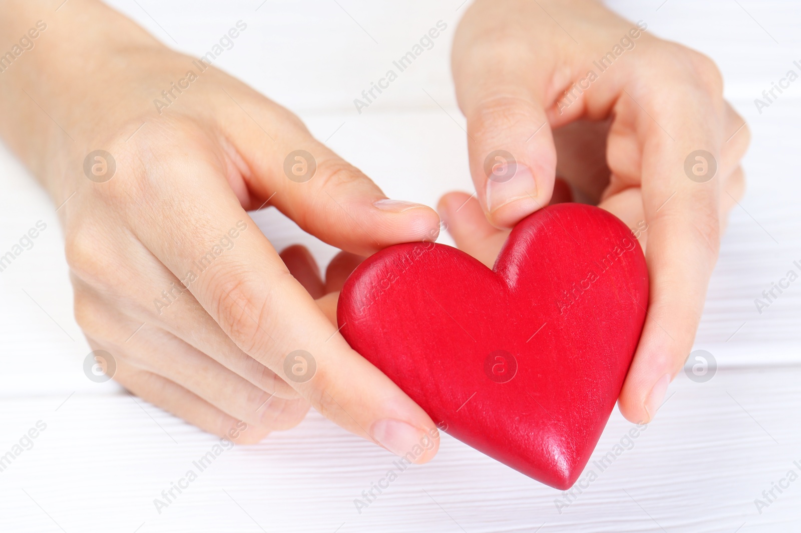 Photo of Woman holding red heart at white wooden table, closeup