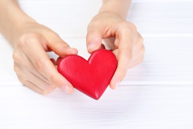 Photo of Woman holding red heart at white wooden table, closeup