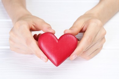 Photo of Woman holding red heart at white wooden table, closeup