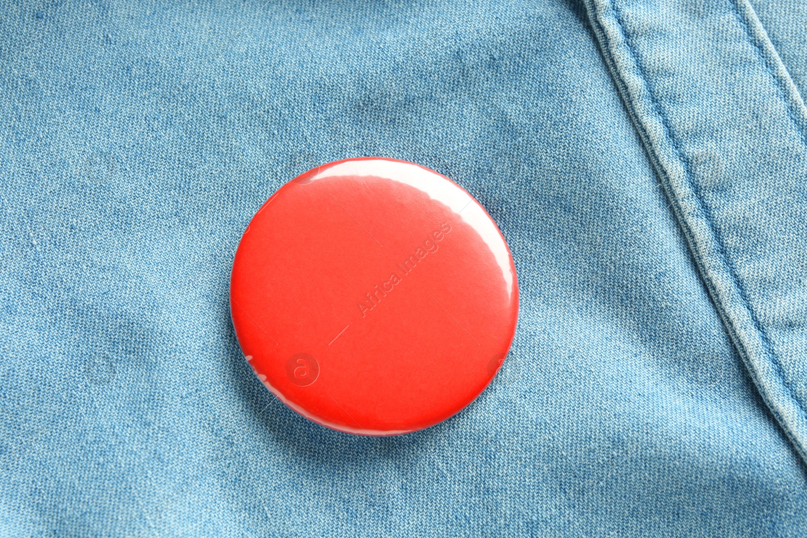 Photo of Red button badge pinned on denim shirt, top view. Mockup for design