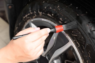 Photo of Man cleaning car wheel with brush indoors, closeup