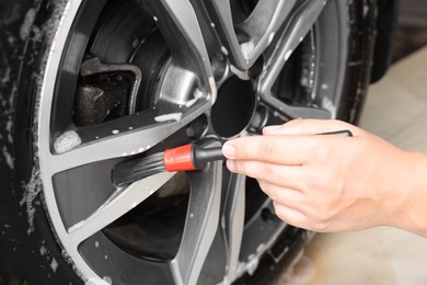 Photo of Man cleaning car wheel with brush indoors, closeup