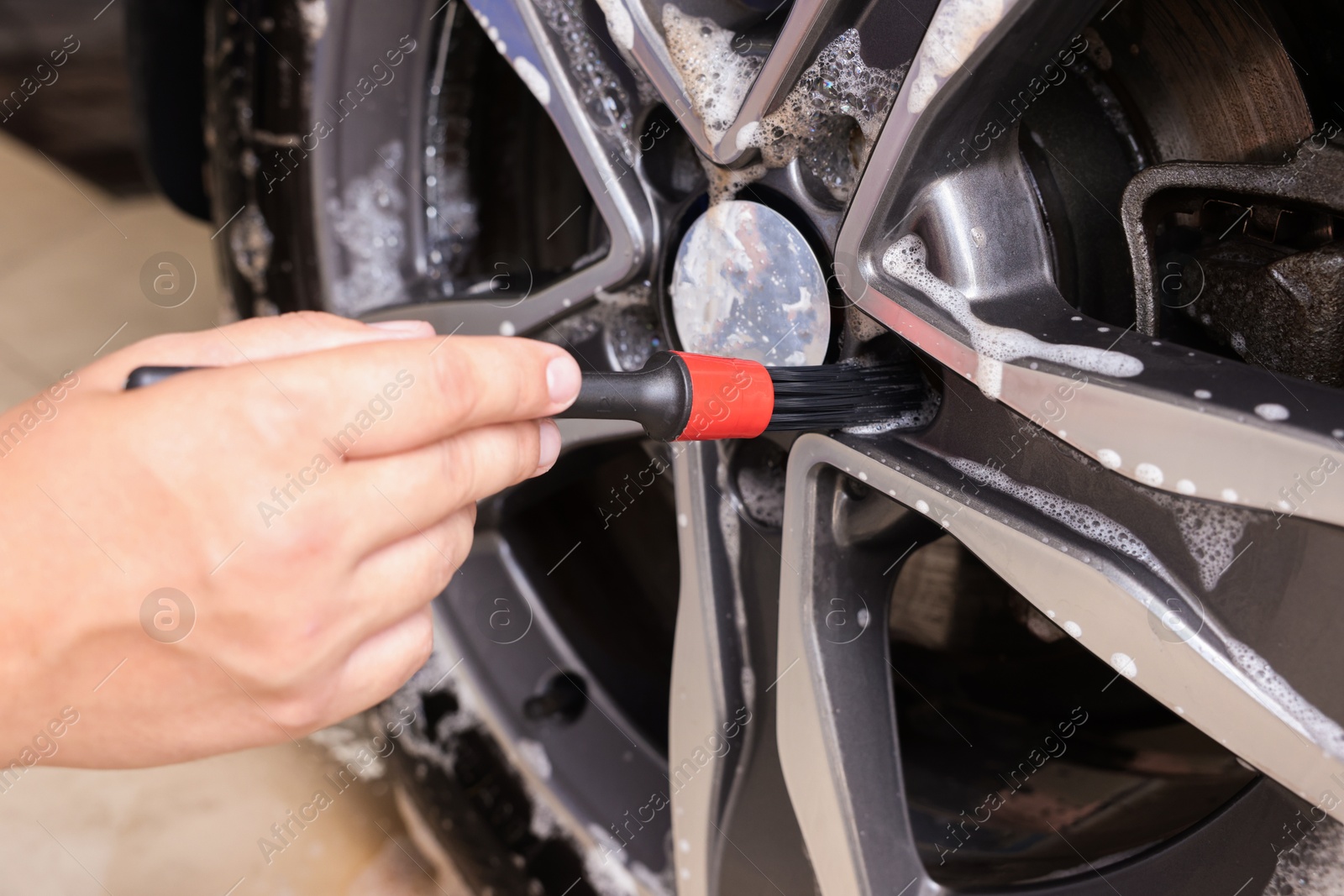 Photo of Man cleaning car wheel with brush indoors, closeup