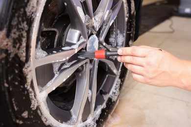 Man cleaning car wheel with brush indoors, closeup