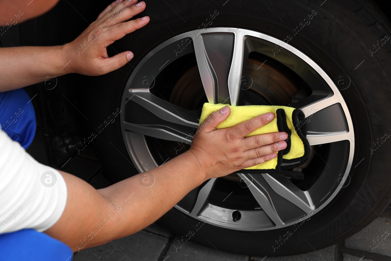 Photo of Man wiping car wheel with yellow rag, closeup