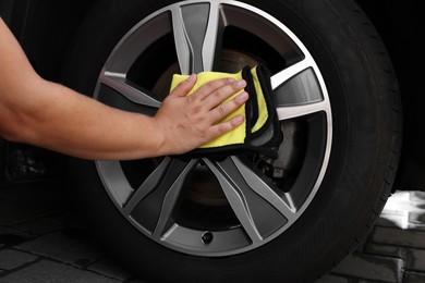 Man wiping car wheel with yellow rag, closeup