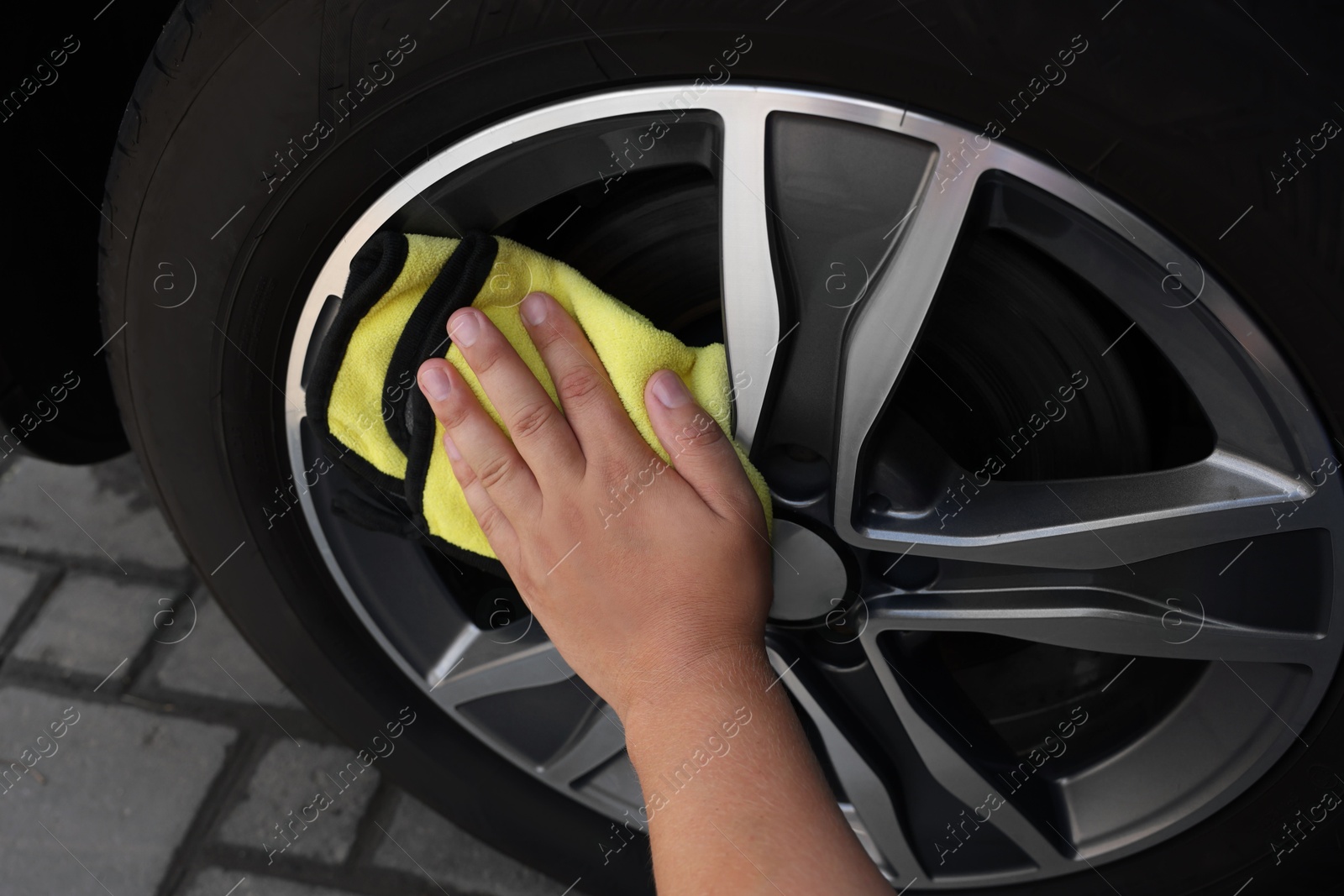 Photo of Man wiping car wheel with yellow rag, closeup