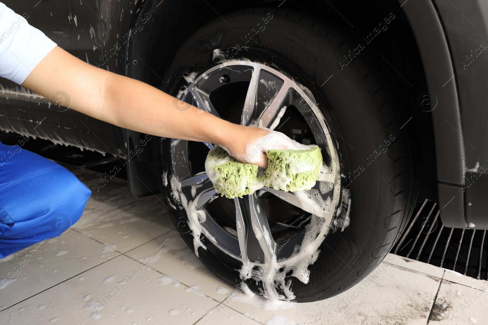 Photo of Man washing car wheel with sponge indoors, closeup