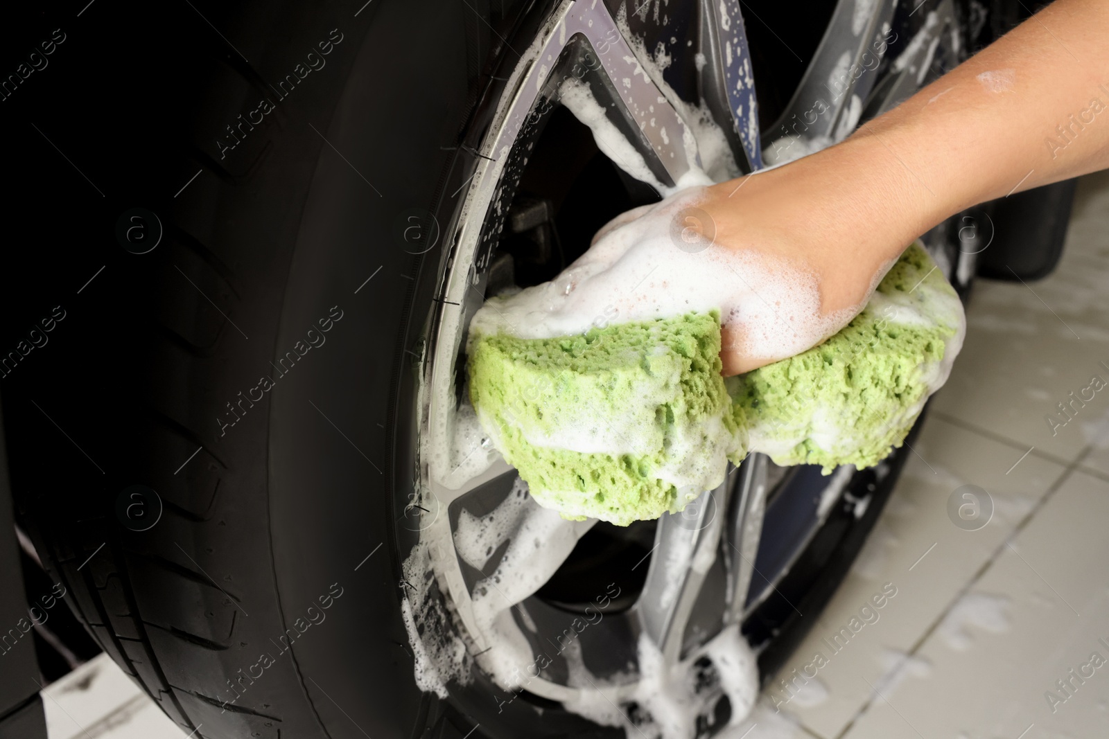 Photo of Man washing car wheel with sponge indoors, closeup