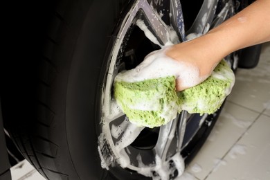 Man washing car wheel with sponge indoors, closeup