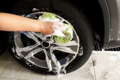 Man washing car wheel with sponge indoors, closeup