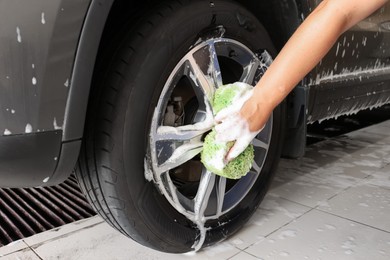 Photo of Man washing car wheel with sponge indoors, closeup