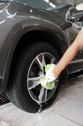 Man washing car wheel with sponge indoors, closeup