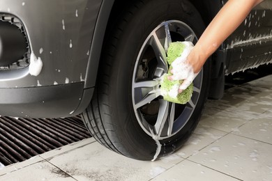 Man washing car wheel with sponge indoors, closeup