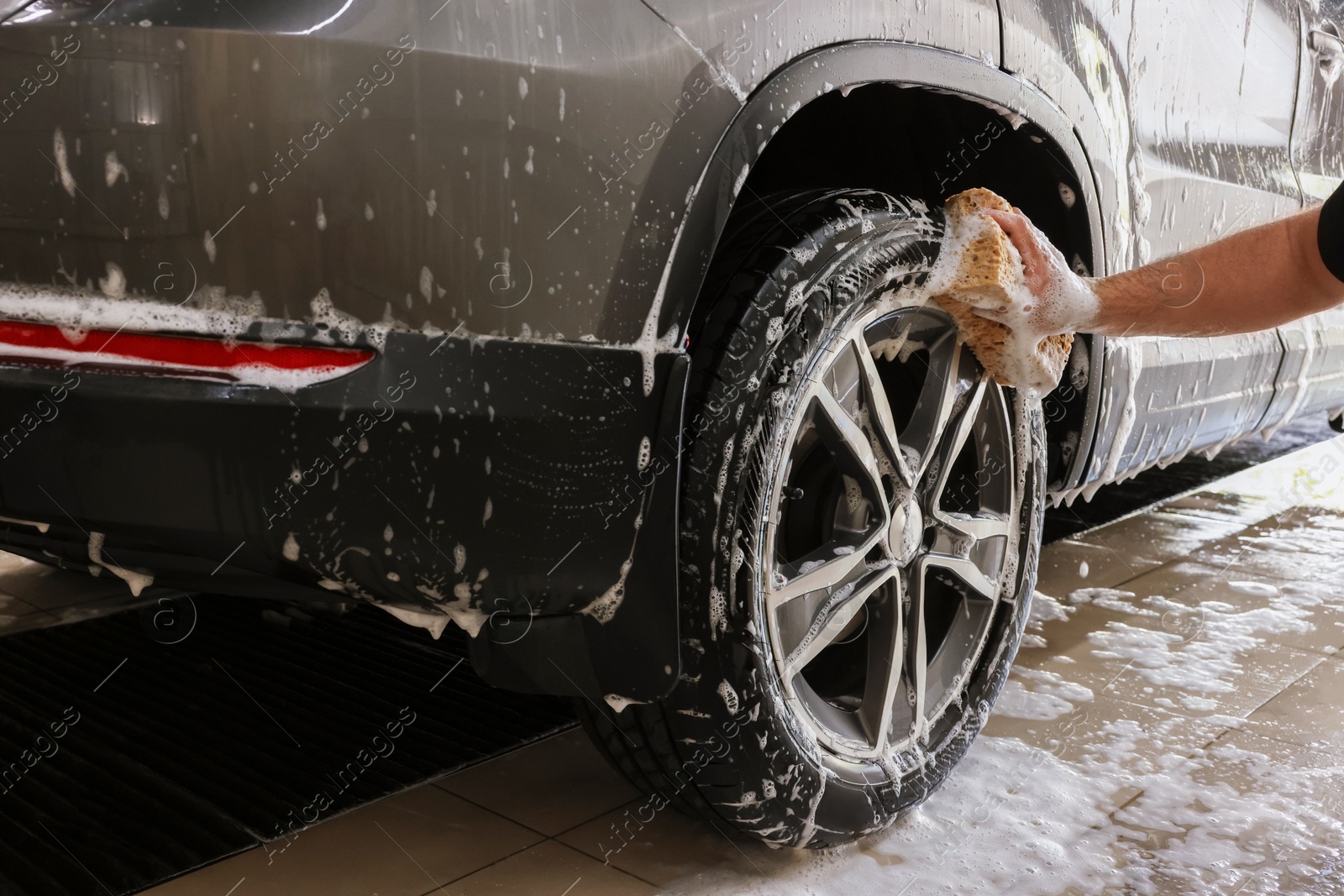 Photo of Man washing car wheel with sponge indoors, closeup