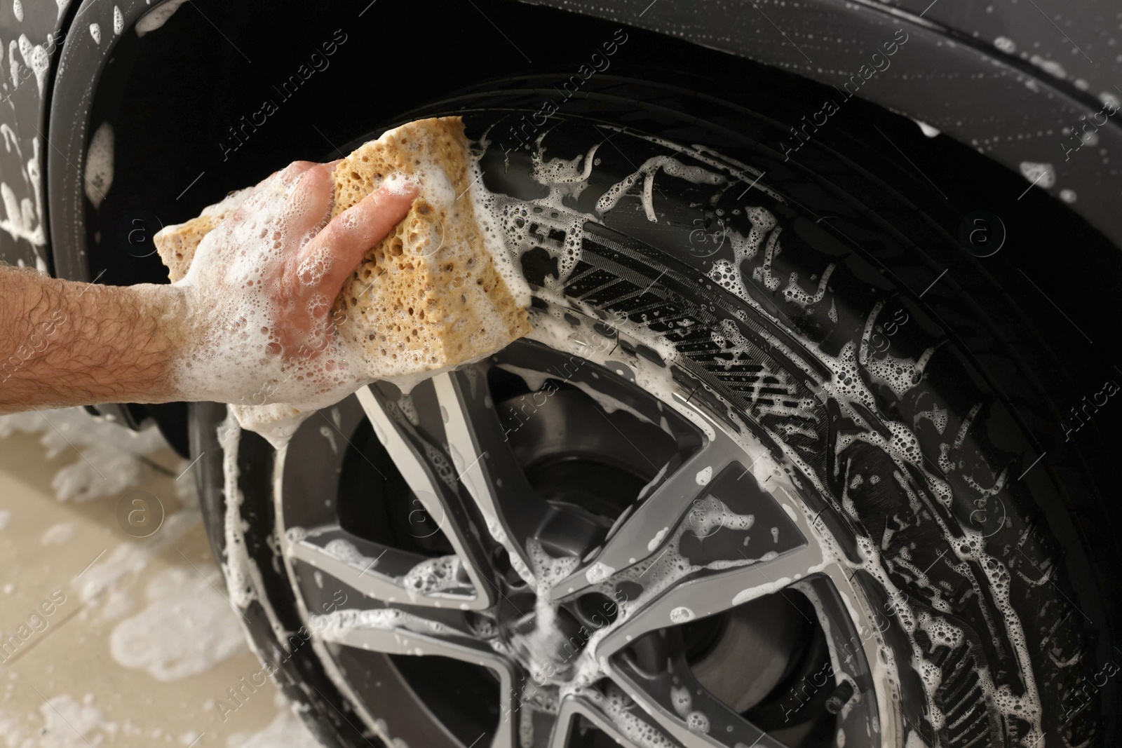 Photo of Man washing car wheel with sponge indoors, closeup