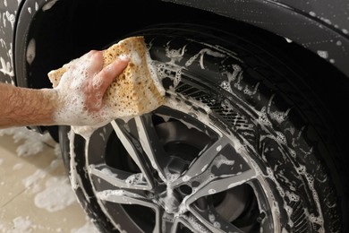 Man washing car wheel with sponge indoors, closeup