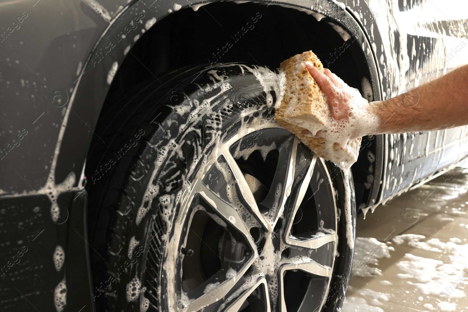 Photo of Man washing car wheel with sponge indoors, closeup