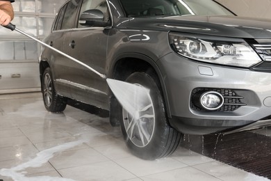 Photo of Man washing auto with high pressure water jet at car wash, closeup