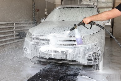 Man washing auto with high pressure water jet at car wash, closeup