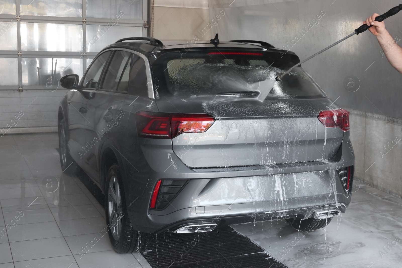 Photo of Man washing auto with high pressure water jet at car wash, closeup