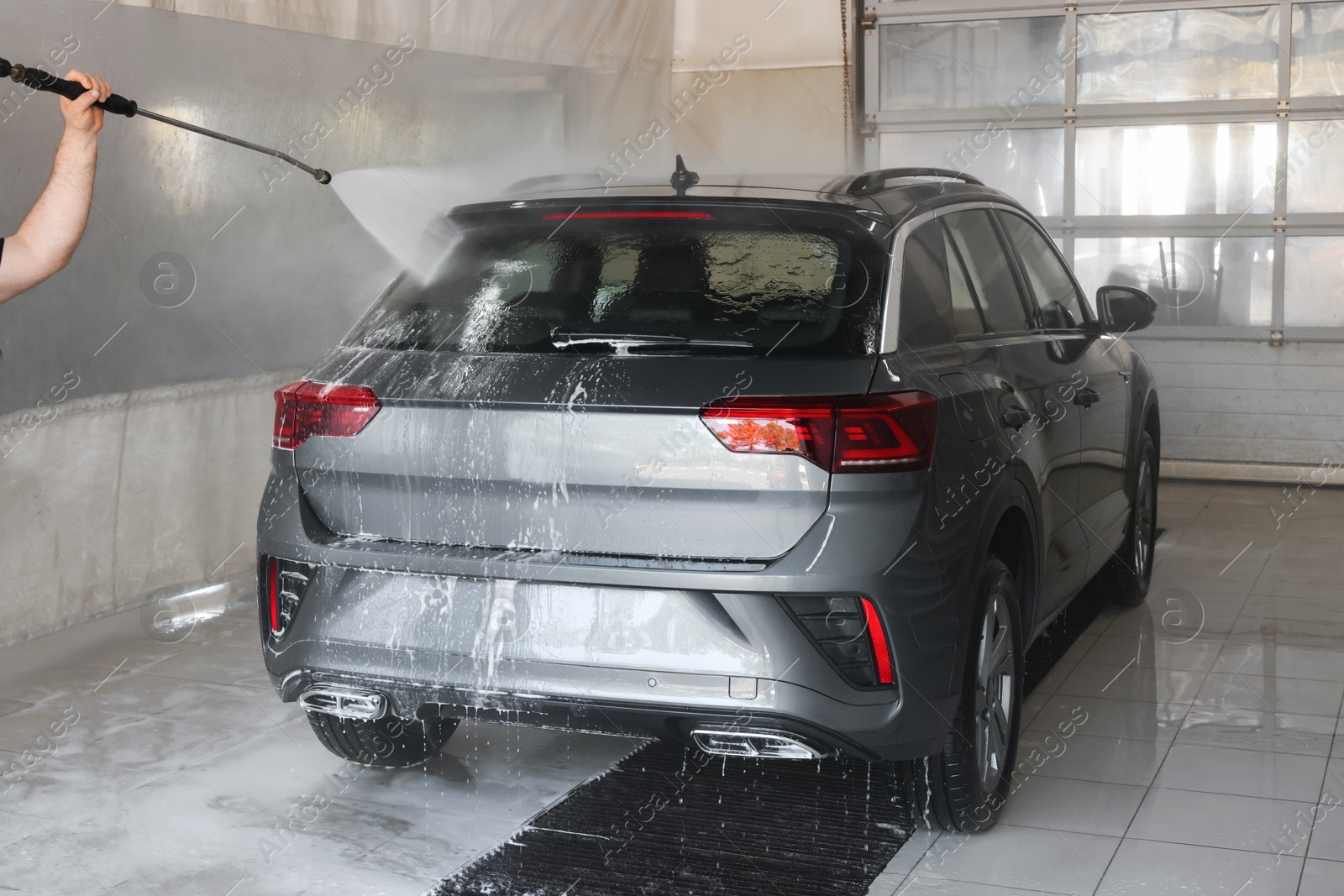 Photo of Man washing auto with high pressure water jet at car wash, closeup