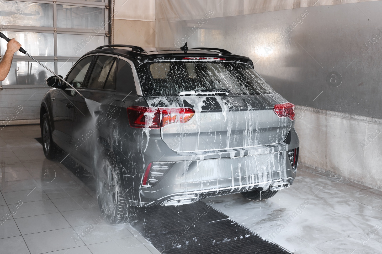 Photo of Man washing auto with high pressure water jet at car wash, closeup