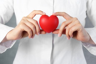 Doctor holding red heart on grey background, closeup