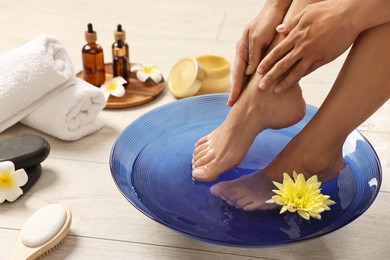 Photo of Woman soaking her feet in bowl with water and flowers on floor, closeup. Body care