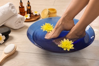 Woman soaking her feet in bowl with water and flowers on floor, closeup. Body care