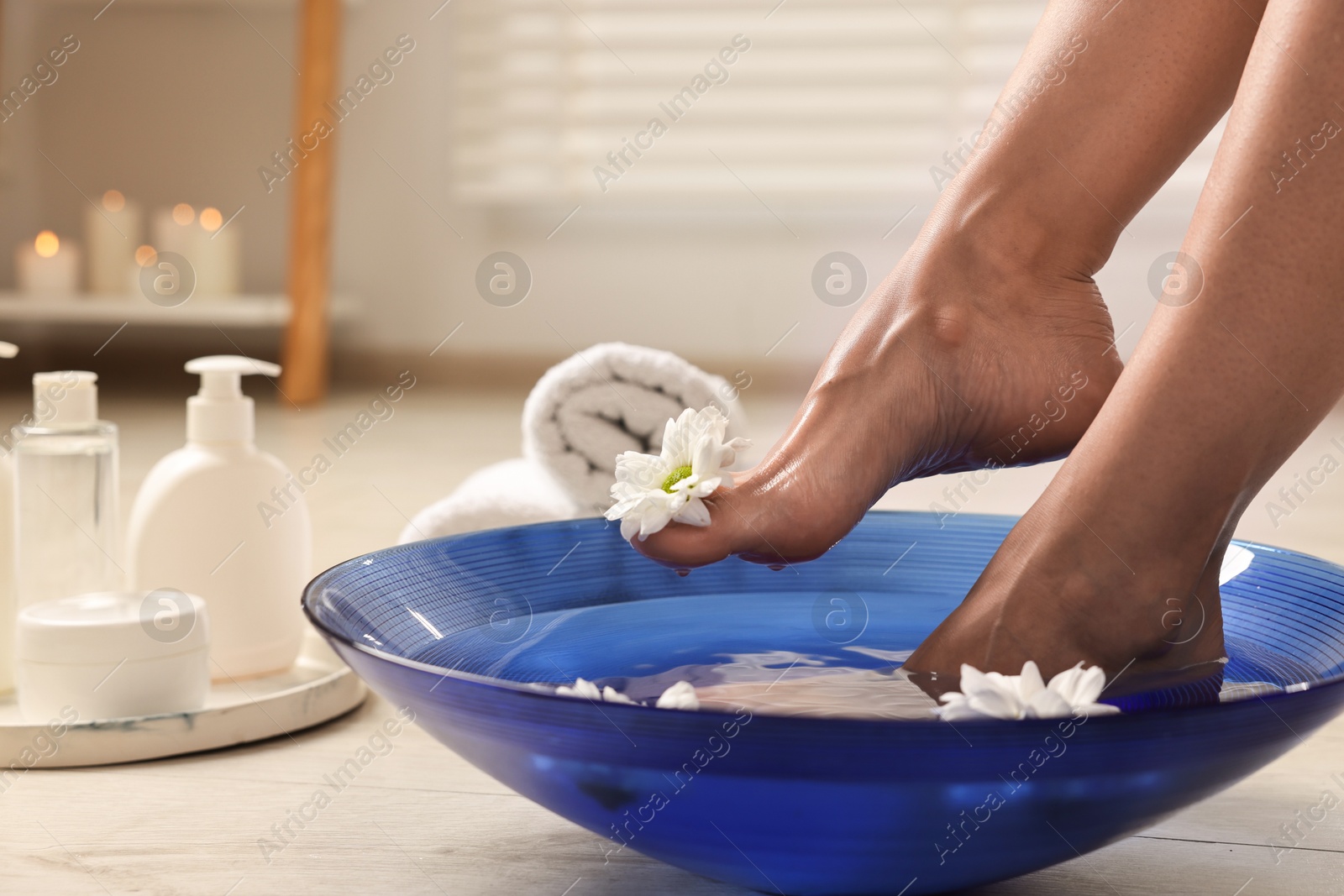 Photo of Woman soaking her feet in bowl with water and flowers on floor, closeup. Body care