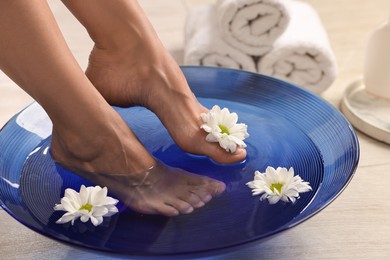 Photo of Woman soaking her feet in bowl with water and flowers on floor, closeup. Body care