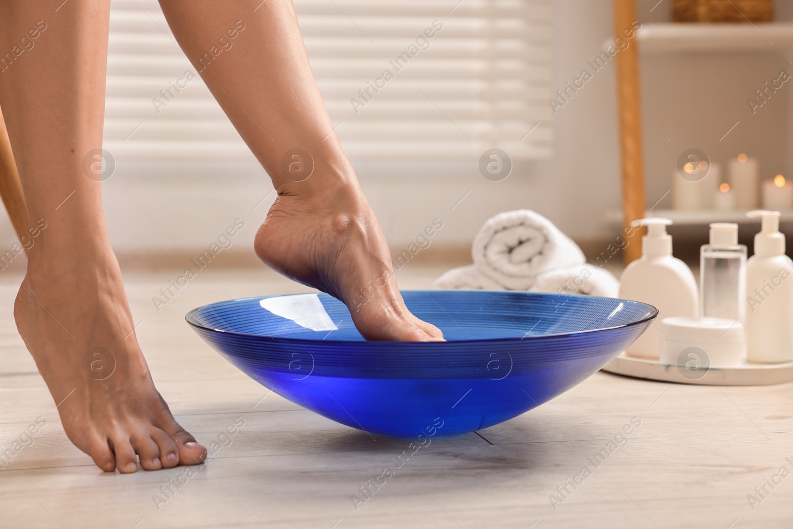 Photo of Woman soaking her feet in bowl with water on floor, closeup. Body care