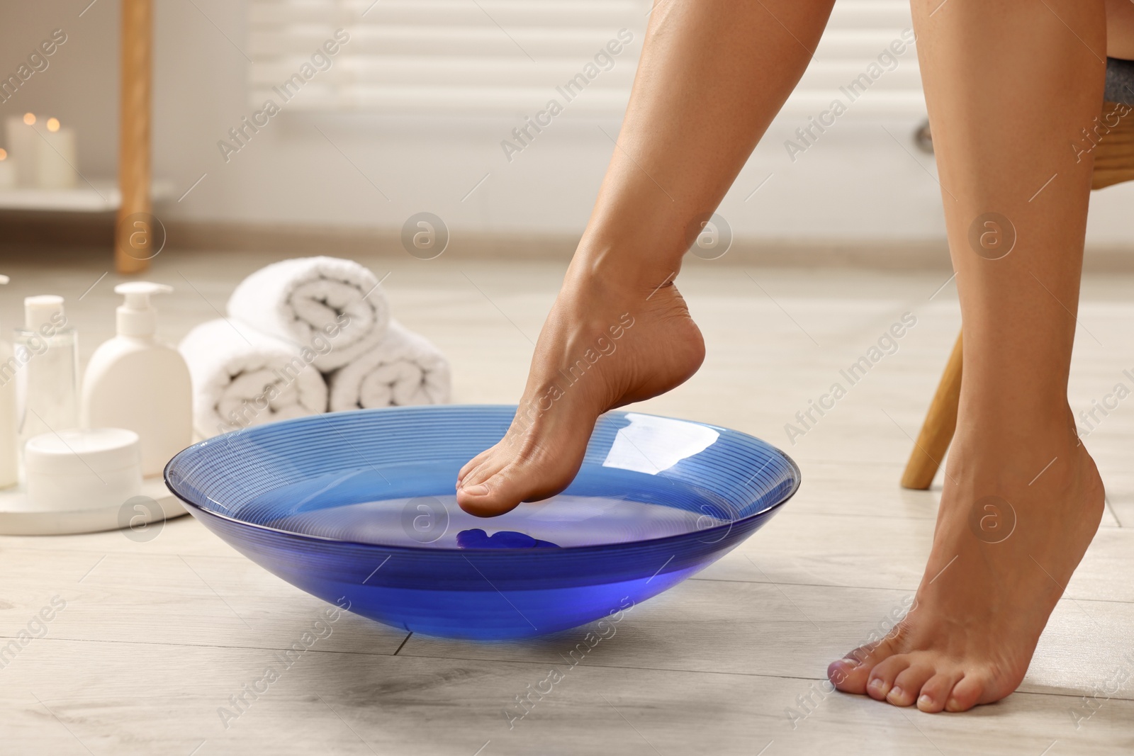 Photo of Woman soaking her feet in bowl with water on floor, closeup. Body care