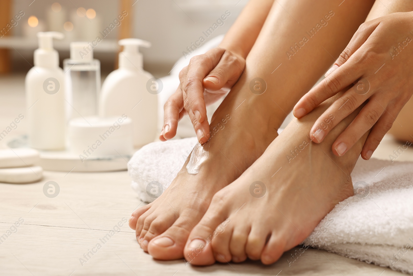 Photo of Woman applying moisturizing cream onto her feet on floor, closeup. Body care