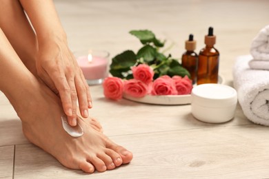 Photo of Woman applying moisturizing cream onto her feet on floor, closeup. Body care