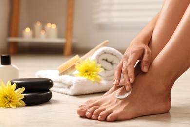 Woman applying moisturizing cream onto her feet on floor, closeup. Body care