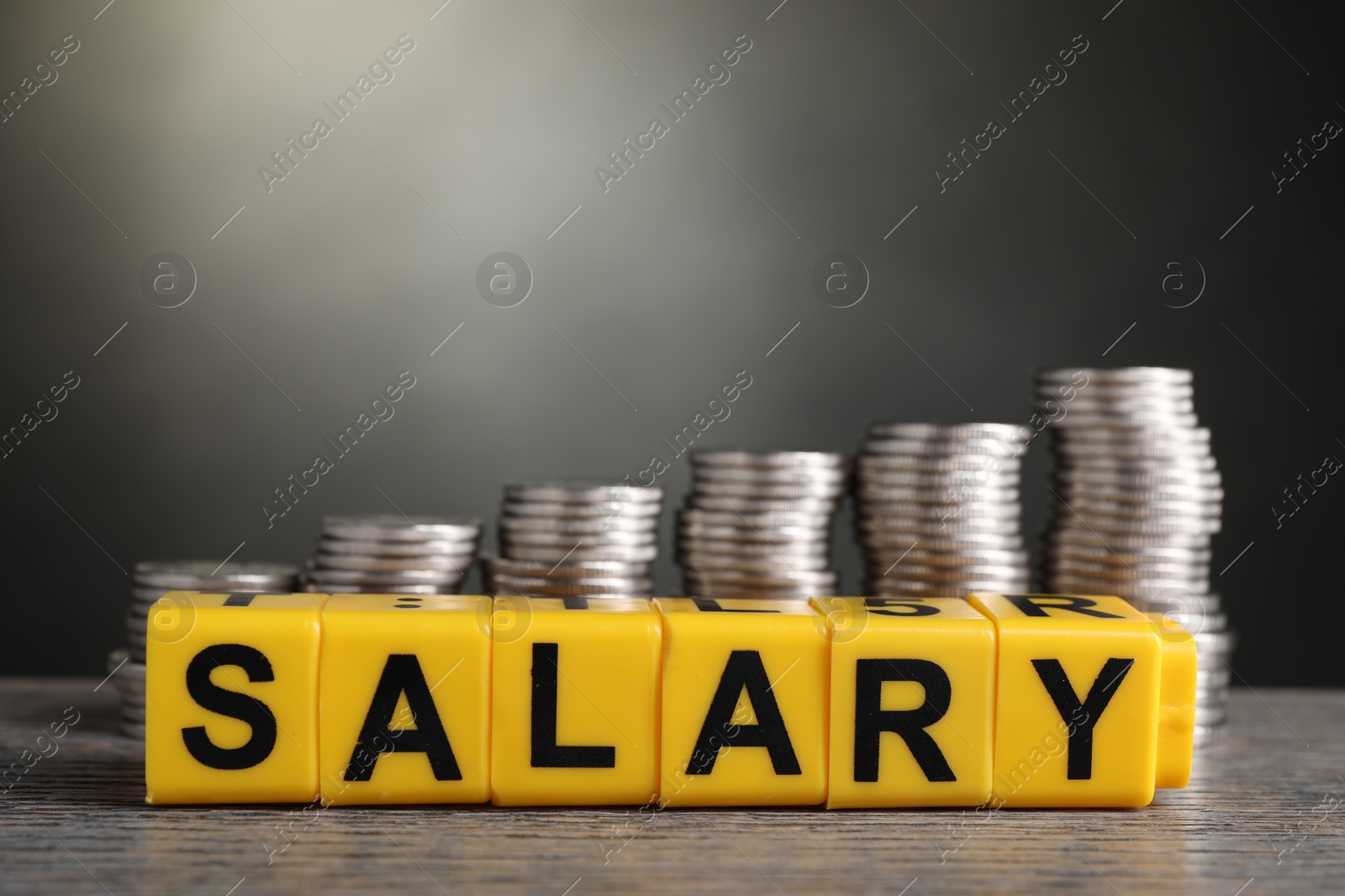 Photo of Word Salary made of cubes and stacked coins on wooden table, closeup