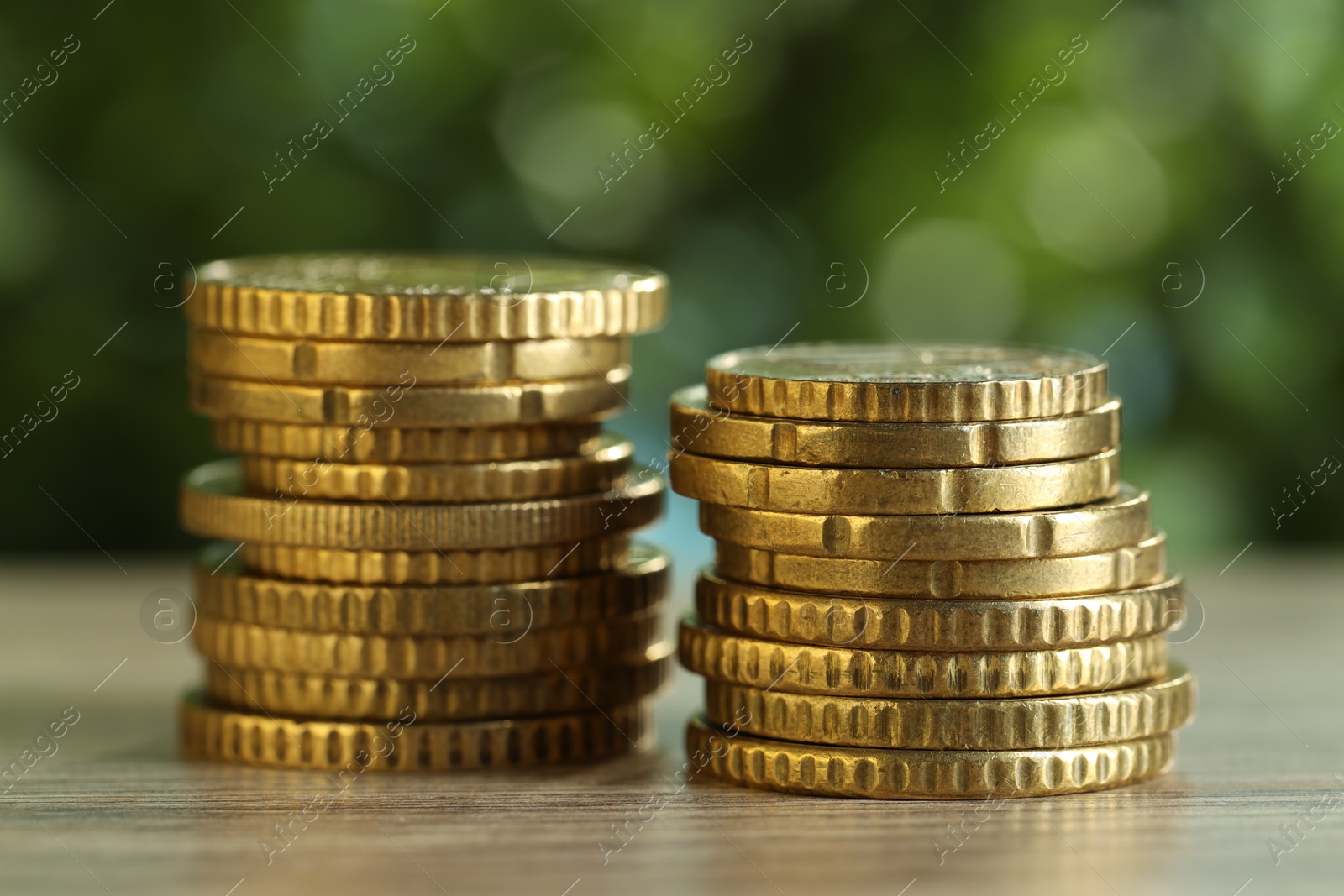 Photo of Stacked coins on light wooden table against blurred green background, closeup. Salary concept