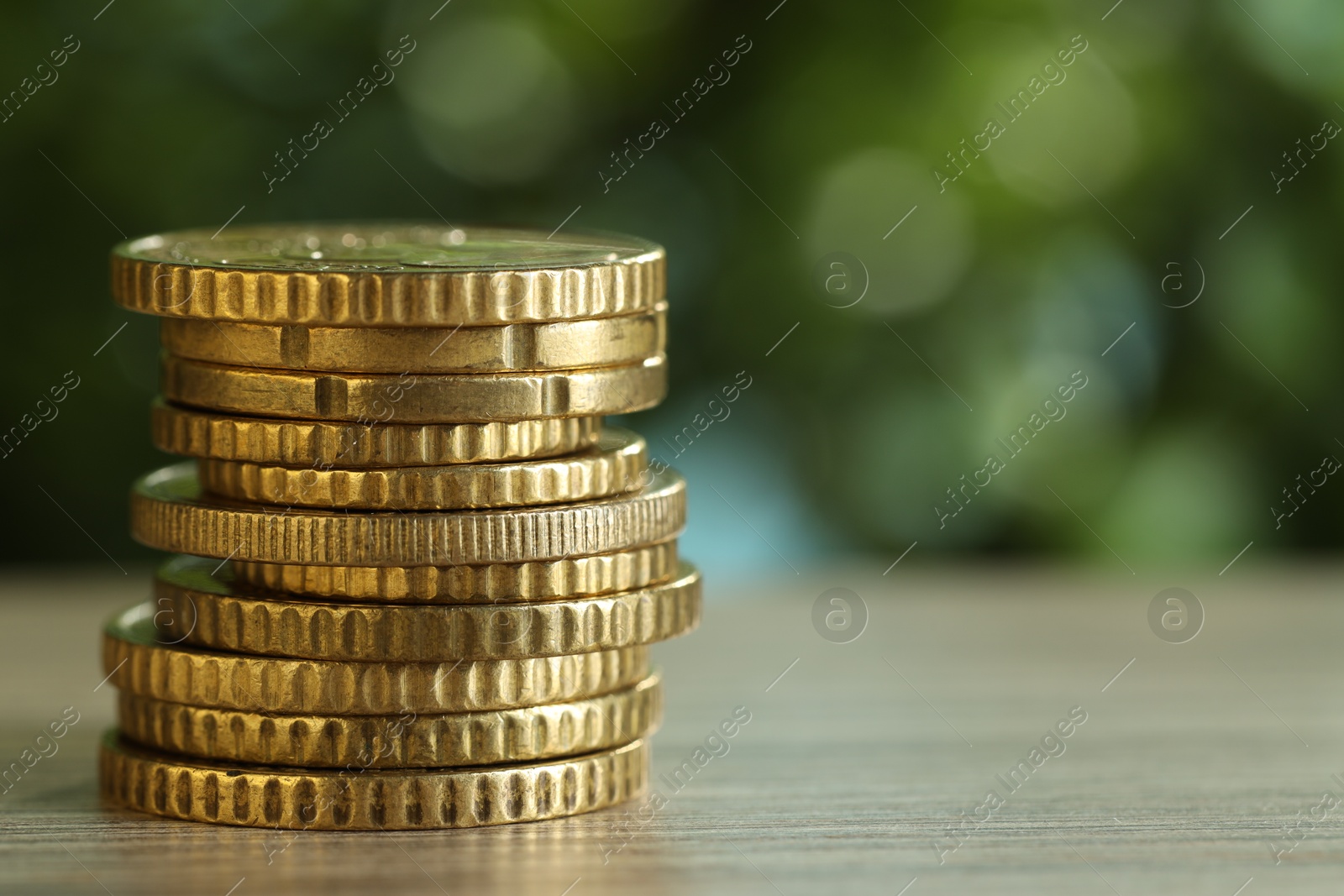 Photo of Stack of coins on light wooden table against blurred green background, closeup with space for text. Salary concept