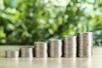 Photo of Stacked coins on light wooden table against blurred green background, closeup. Salary concept