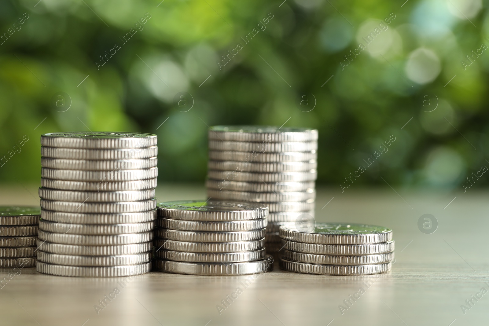 Photo of Stacked coins on light wooden table against blurred green background, closeup. Salary concept