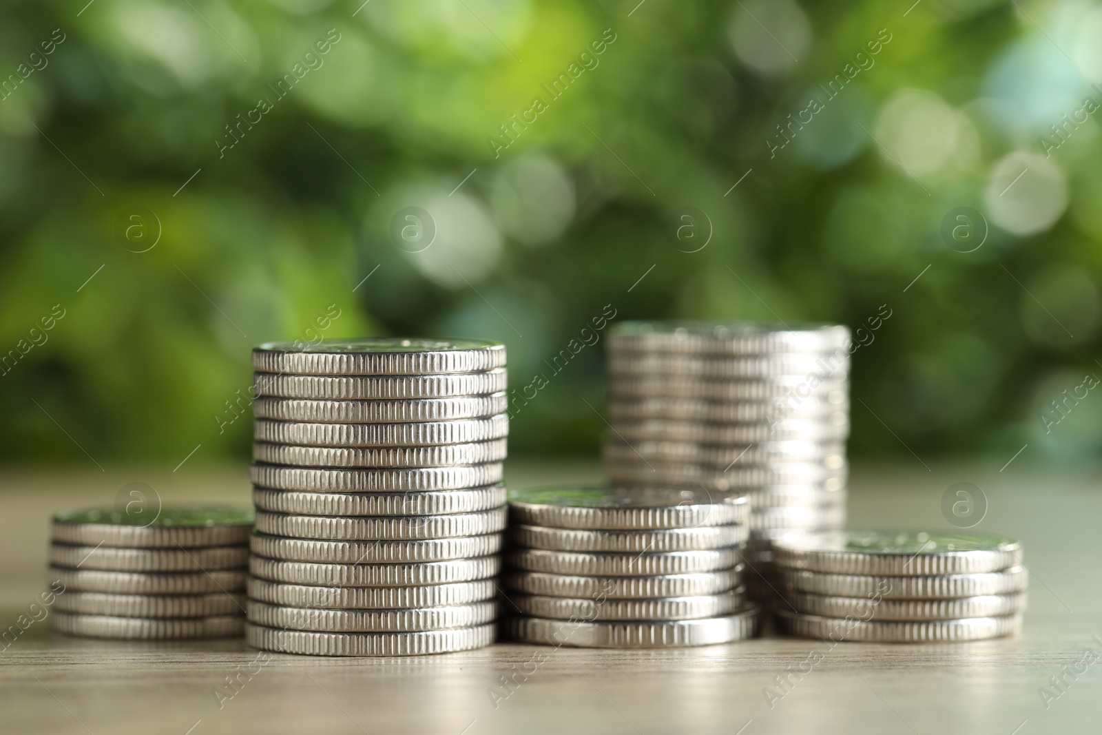 Photo of Stacked coins on light wooden table against blurred green background, closeup. Salary concept