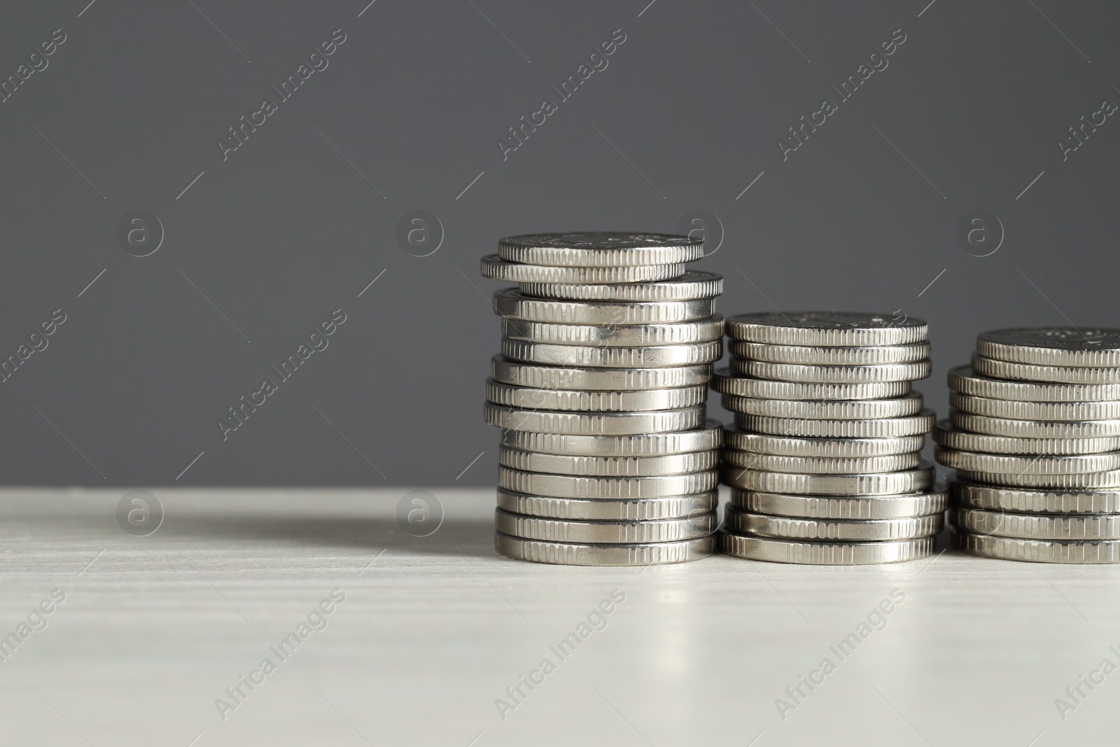 Photo of Stacked coins on white wooden table against grey background, space for text. Salary concept