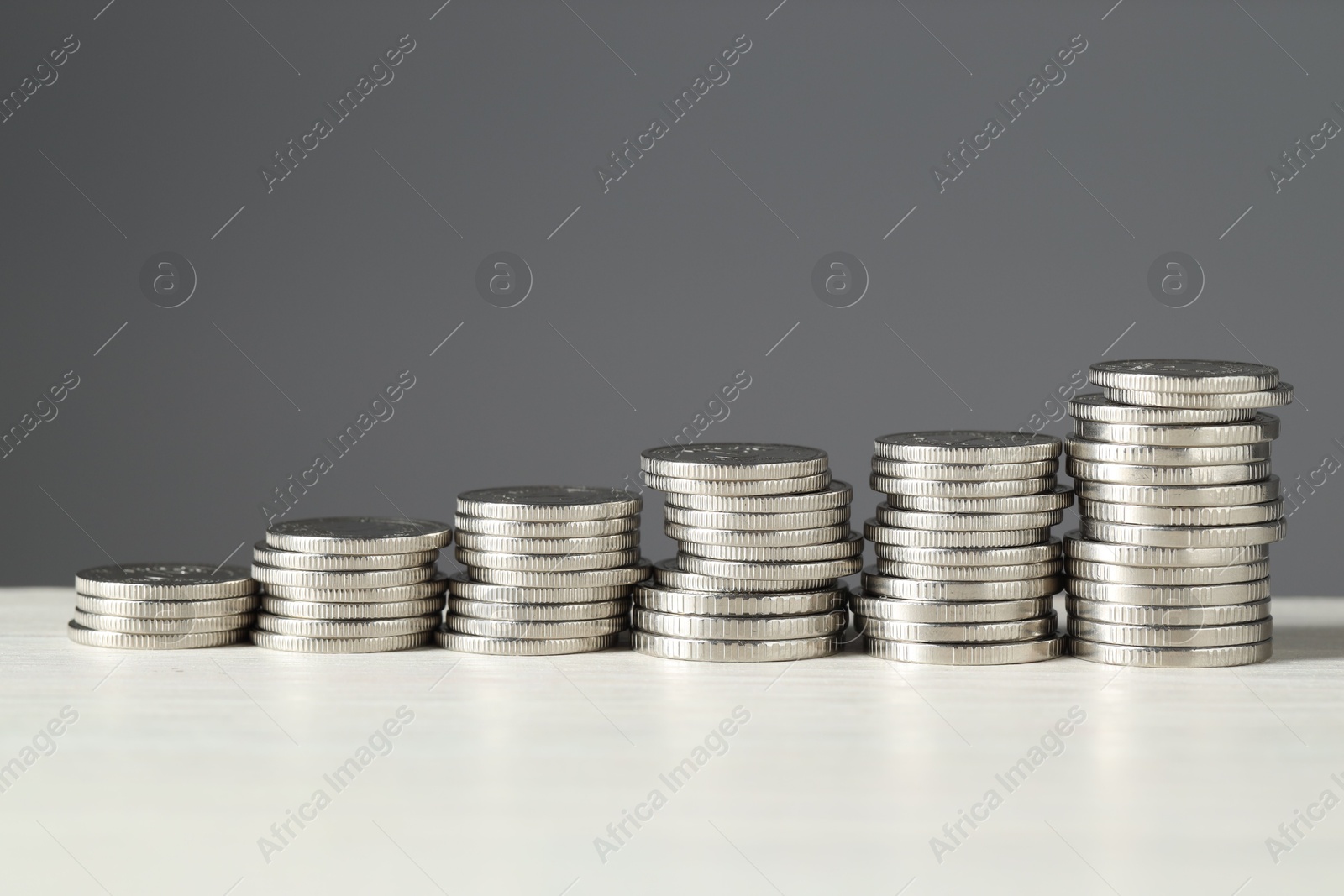 Photo of Stacked coins on white wooden table against grey background, closeup. Salary concept