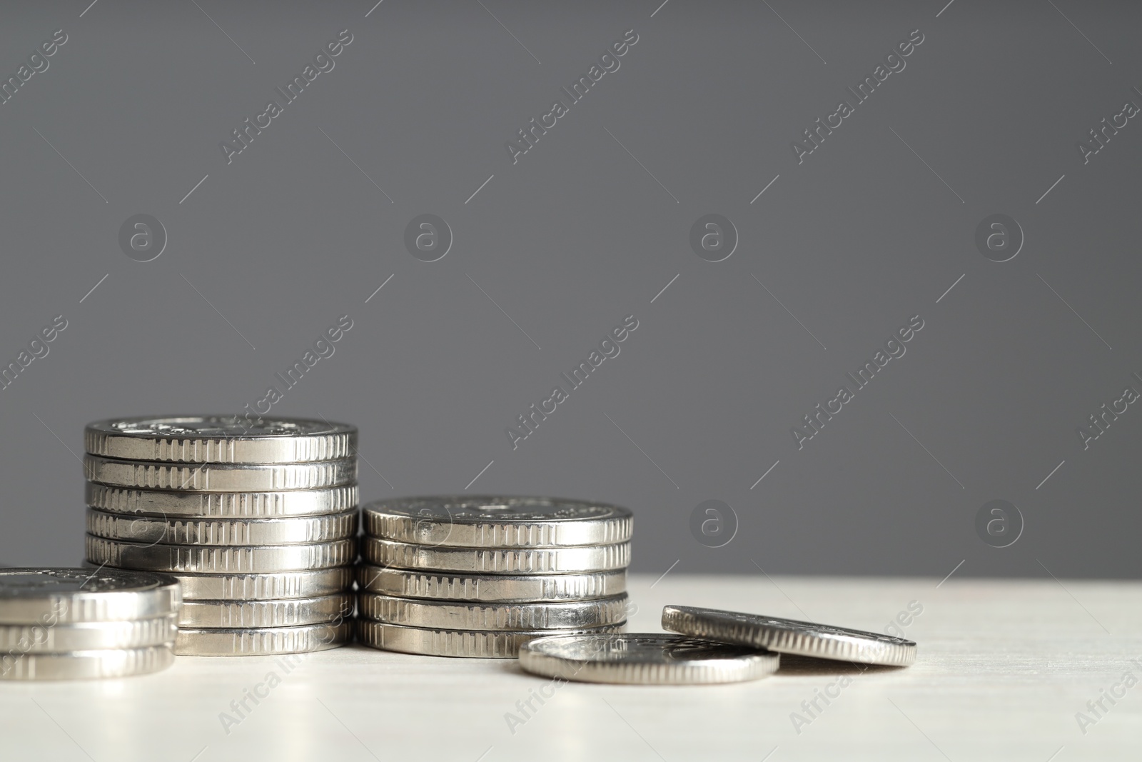 Photo of Stacked coins on white wooden table against grey background, closeup with space for text. Salary concept