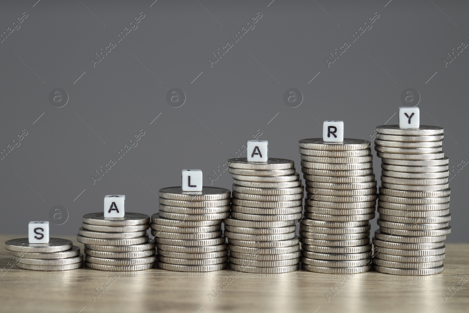 Photo of Word Salary made of cubes and stacked coins on wooden table against grey background