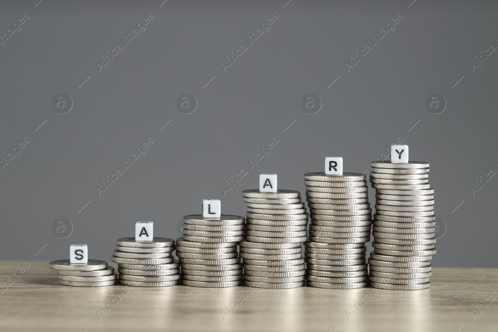 Photo of Word Salary made of cubes and stacked coins on wooden table against grey background